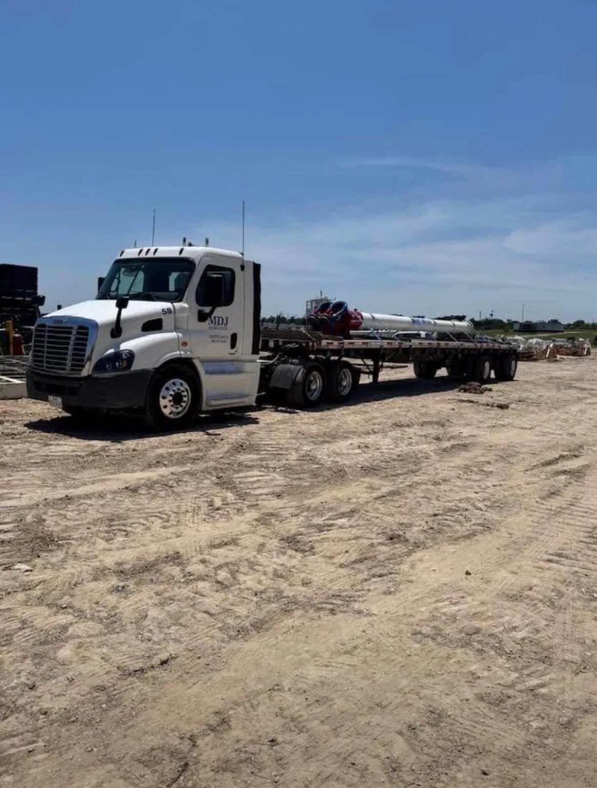 MDJ Services flatbed truck hauling bundled pipe on a dirt jobsite in Southeast Texas